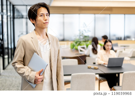 パソコンを小脇に抱えて斜め左方向に体を向けて立っているビジネスマン パソコンを小脇に抱えて斜め左方向に体を向けて立っているビジネスマン 119039968