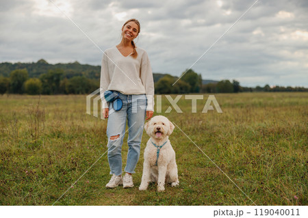 A woman enjoying a peaceful walk with her dog in a beautiful scenic field, surrounded by nature 119040011