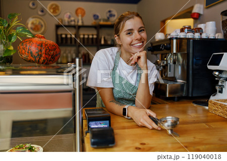 A friendly barista with a warm smile greets customers, enhancing the cozy coffee shop 119040018
