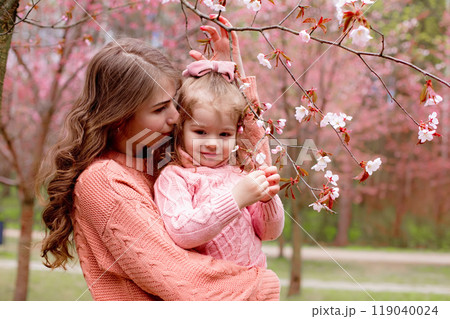 mother and little girl , hugging in the park with blooming pink sakura. 119040024