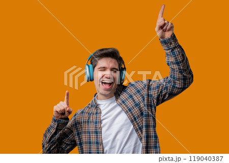 Young positive man listening music, enjoying with headphones, yellow studio Young positive man listening music, enjoying with headphones, yellow studio 119040387