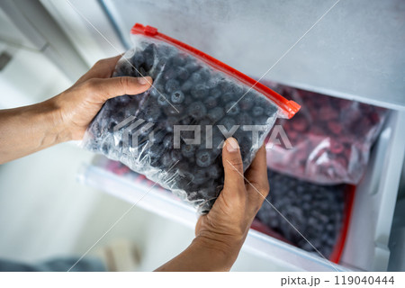 Hands hold zip bag with blueberries, putting into freezer. Cost effective frozen food storage 119040444