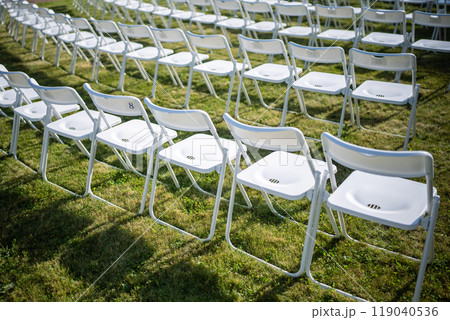 Folding chairs standing in row on green grass, casting shadow on ground. Outdoor party preparation Folding chairs standing in row on green grass, casting shadow on ground. Outdoor party preparation 119040536