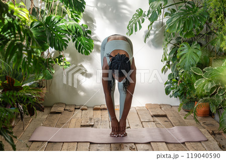 Fitness black girl do forward bend stretching warms up muscles before sports training in plants room Fitness black girl do forward bend stretching warms up muscles before sports training in plants room 119040590