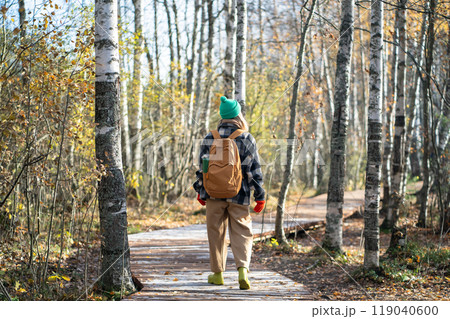 Rear view tourist woman with backpack walking on forest eco path on autumn cold day in warm clothes 119040600