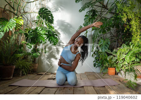 Healthy body with fitness. Active african american woman stretching hand aside sitting on sports mat 119040602