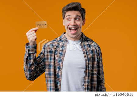 Successful man in orange polo shirt showing unlimited gold credit card on yellow studio background. Student, money concept. 119040619
