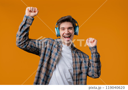 Young positive man listening music, enjoying with headphones, yellow studio 119040620