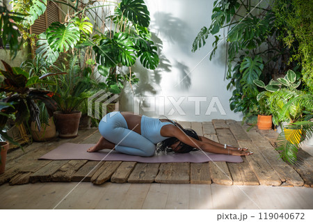 Black sportswoman lying on fitness mat do stretching exercise relaxing back muscles in urban jungle. Black sportswoman lying on fitness mat do stretching exercise relaxing back muscles in urban jungle. 119040672
