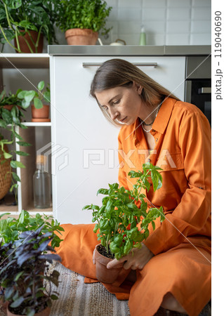 Interested woman tends home seedlings herbs by sit on floor focusing on interacting with houseplants Interested woman tends home seedlings herbs by sit on floor focusing on interacting with houseplants 119040690