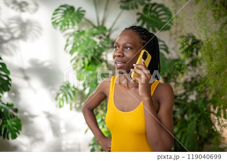 Interested pensive black girl make call conversation with cellphone surround by tropical houseplants 119040699