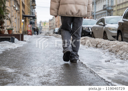 Person walking on slippery sidewalk rear view. Pavement covered with slippery ice. Frozen rain.  119040729