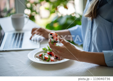 Woman eats healthy snack of rye crisp bread with cherry tomatoes and cream cheese while using laptop Woman eats healthy snack of rye crisp bread with cherry tomatoes and cream cheese while using laptop 119040736