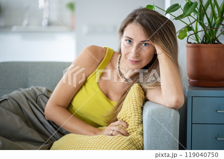 Relaxed woman sitting on sofa spending lazy time at home look at camera with calm emotion. Slow life Relaxed woman sitting on sofa spending lazy time at home look at camera with calm emotion. Slow life 119040750