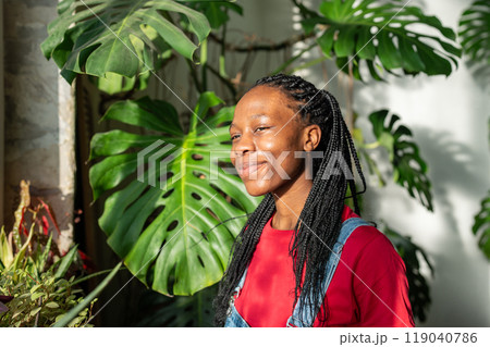 Pleased African American young woman stands by window, basking in sunlight with smile face feel joy. Pleased African American young woman stands by window, basking in sunlight with smile face feel joy. 119040786
