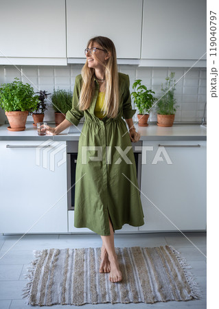 Happy smiling relaxed woman daydreaming enjoy life looking at window standing in kitchen with plants 119040797