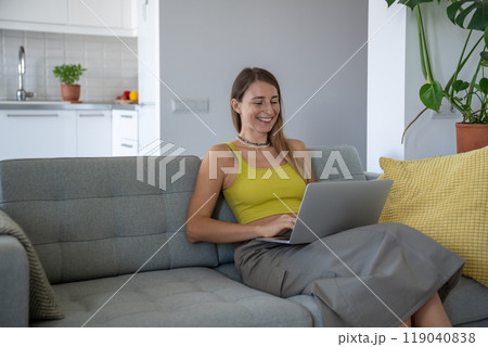 Interested woman smiling using laptop on knees chatting online internet social network on home sofa. Interested woman smiling using laptop on knees chatting online internet social network on home sofa. 119040838