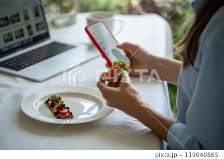 Hand holding bread cracker topped with cream cheese, tomatoes, fresh herbs take breakfast with phone 119040865