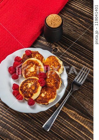 Cottage cheese pancakes with fresh raspberries on a white plate on the table 119041401