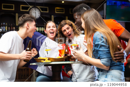 Excited diverse football supporters with flag of France watching tournament with beer and snacks in the pub 119044958
