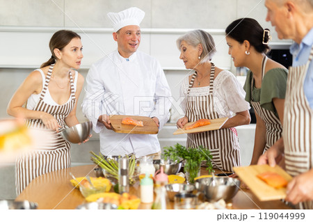 Chef in uniform teaches cooking class students how to clean and cut salmon fillet 119044999