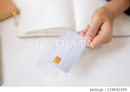 A top view of a woman's hand holding a credit card over a white table. A top view of a woman's hand holding a credit card over a white table. 119045394