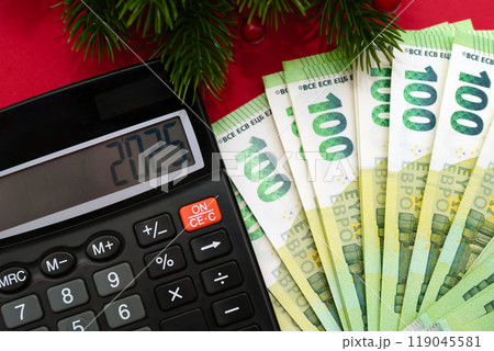 Calculator, 100 euro banknotes and the inscription 2025 new year with spruce branches on a red background, economic crisis, tax time Calculator, 100 euro banknotes and the inscription 2025 new year with spruce branches on a red background, economic crisis, tax time 119045581