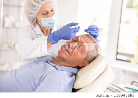 Doctor performs procedure of injectable correction of wrinkles in nasal bridge area for man Doctor performs procedure of injectable correction of wrinkles in nasal bridge area for man 119045698