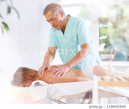 Skilled old masseur conducting back massage for woman client Skilled old masseur conducting back massage for woman client 119045840