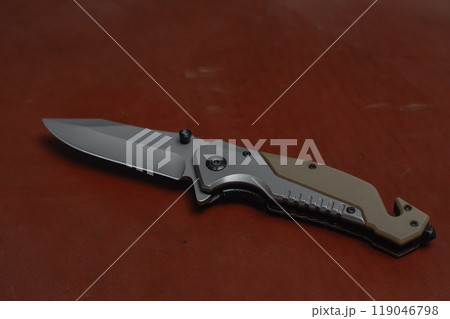 An unfolded tactical military knife with a sharp blade. Tool against the natural leather. 119046798
