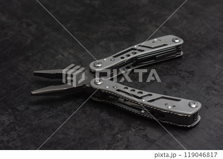 Tactical outdoor multi-tool with pliers, blade, screwdriver and other tools on a dark concrete background. Universal multitool for tourism and repair. Tactical outdoor multi-tool with pliers, blade, screwdriver and other tools on a dark concrete background. Universal multitool for tourism and repair. 119046817