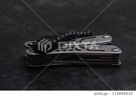 Tactical outdoor multi-tool with pliers, blade, screwdriver and other tools on a dark concrete background. Universal multitool for tourism and repair. Tactical outdoor multi-tool with pliers, blade, screwdriver and other tools on a dark concrete background. Universal multitool for tourism and repair. 119046818