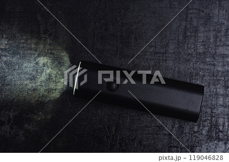Small black bicycle light with a beam of light, rests on a dark table. 119046828