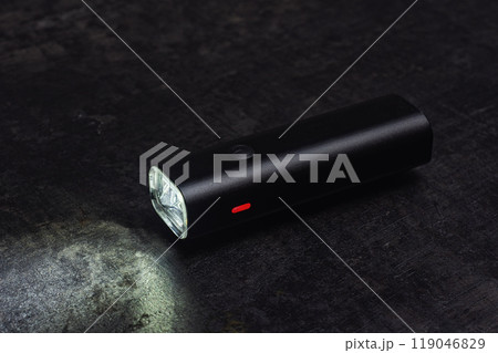 Small black bicycle light with a beam of light, rests on a dark table. Small black bicycle light with a beam of light, rests on a dark table. 119046829