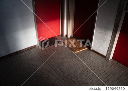 A serene hallway with red doors, featuring doormats on tiled floors softly illuminated by natural light, creating a warm and welcoming ambience. A serene hallway with red doors, featuring doormats on tiled floors softly illuminated by natural light, creating a warm and welcoming ambience. 119049260