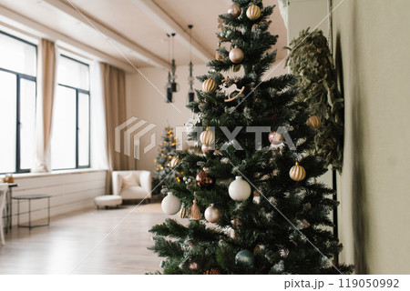 Large Christmas tree with many ornaments sits in a room with a window 119050992