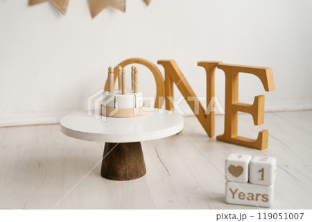 White wooden toy cake on a stand in front of a sign with the inscription one. First children's birthday 119051007
