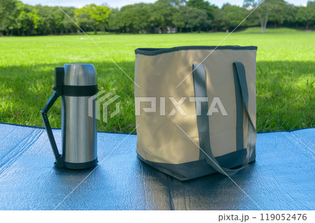 芝生のある公園にレジャーシートと水筒と保冷バッグが置かれている　 119052476