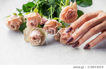 Elegant hand with dark manicure resting beside delicate pink roses on a light surface Elegant hand with dark manicure resting beside delicate pink roses on a light surface 119053029