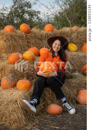 Woman holding a pumpkin sitting on hay bales 119053145
