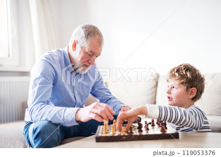 Grandpa teaching young boy to play chess. Grandfather spending time with grandson, taking care of him while parents are at work. Grandpa teaching young boy to play chess. Grandfather spending time with grandson, taking care of him while parents are at work. 119053376