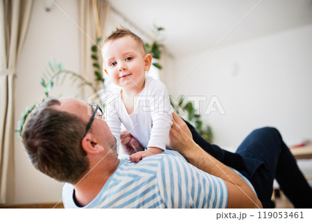 Portrait of father playing with little son, lying on floor and holding small boy above him. 119053461