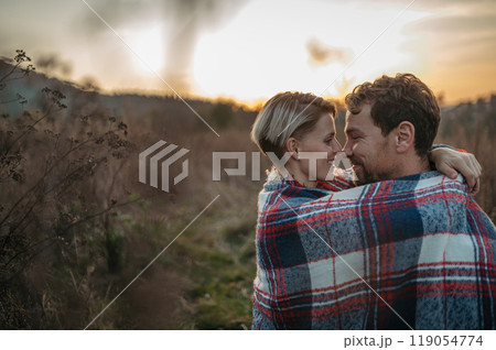 Couple in love on a walk in autumn forest. Husband and wife standing in the middle of meadow covered in warm blanket. Couple in love on a walk in autumn forest. Husband and wife standing in the middle of meadow covered in warm blanket. 119054774