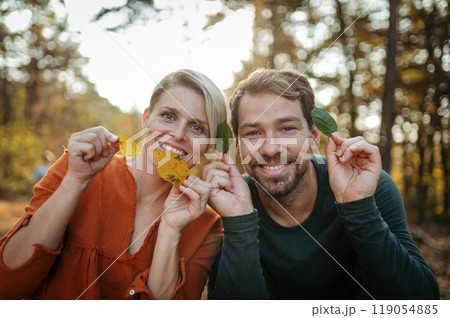 Couple holding colorful leaves, looking at camera. Man and woman on walk in autumn forest. Couple holding colorful leaves, looking at camera. Man and woman on walk in autumn forest. 119054885