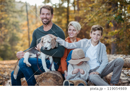 Portrait of family sitting in the middle autumn forest. Nuclear family with dog spending weekend outdoors. 119054989