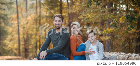 Portrait of family sitting in the middle autumn forest. Nuclear family spending weekend outdoors. Banner with copy space. 119054990