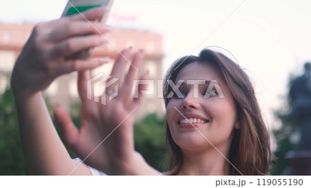 Carefree beautiful woman holding mobile phone, looking at mobile phone screen, using smartphone apps, posing for selfie outdoors. Carefree beautiful woman holding mobile phone, looking at mobile phone screen, using smartphone apps, posing for selfie outdoors. 119055190