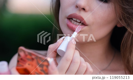 Close-up portrait of a beautiful woman who paints her lips with lipstick outdoors, looking into a pocket mirror. She makes a sexy face. Close-up portrait of a beautiful woman who paints her lips with lipstick outdoors, looking into a pocket mirror. She makes a sexy face. 119055213