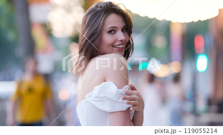 Portrait of a beautiful young woman in a cute white dress on a city street in the evening 119055214