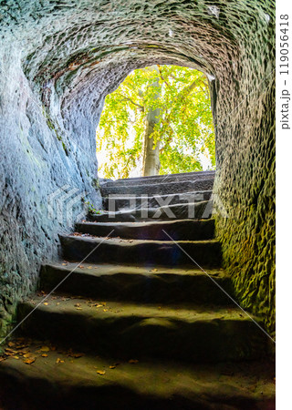 Visitors navigate the ancient stone steps leading out of Frydstejn Castle ruins in Bohemian Paradise, surrounded by lush greenery and historical architecture. 119056418